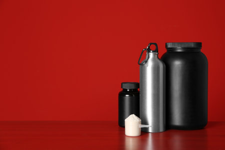 Composition with protein powder and black jars on table against red backgroundの写真素材