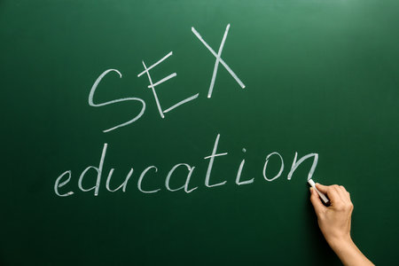 Woman writing phrase "SEX EDUCATION" on green chalkboardの写真素材