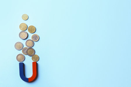 Red and blue horseshoe magnet attracting coins on light blue background, flat lay. Space for textの写真素材