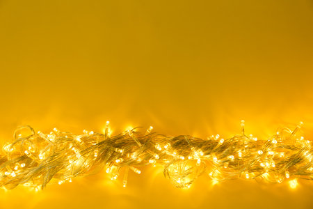 Glowing Christmas lights on yellow background, top view. Space for textの写真素材