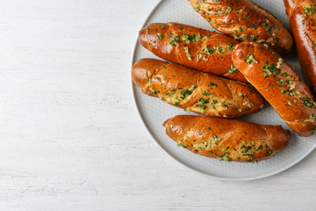 Plate of bread loaves with garlic and herbs on white wooden table, top view. Space for text