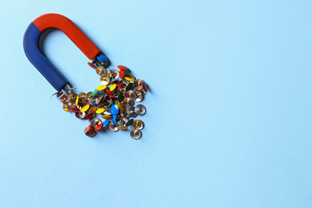 Red and blue horseshoe magnet attracting push pins on light blue background, flat lay. Space for textの写真素材