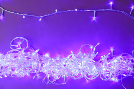 Glowing Christmas lights on violet background, top view