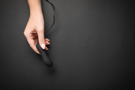Young woman holding little vibrator and charging cable on black background, top view with space for text. sex toyの写真素材