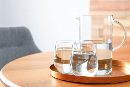 Tray with jug and glasses of water on wooden table in room, space for text. Refreshing drinksの写真素材