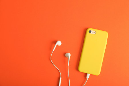 Modern phone with earphones on coral background, top view. Space for textの写真素材