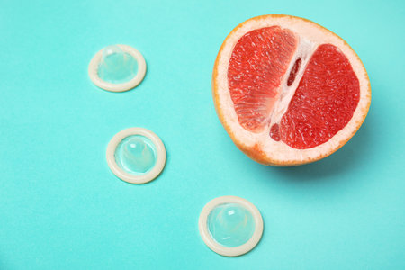 Half of grapefruit and condoms on turquoise background, above view. sex conceptの写真素材