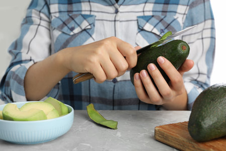 Woman peeling ripe avocado at table, closeupの写真素材