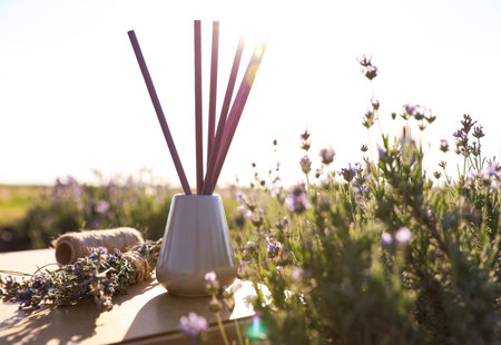 Reed air freshener on wooden table in blooming lavender fieldの写真素材