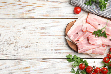 Flat lay composition with sliced raw bacon on white wooden table. Space for textの写真素材