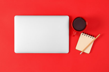 Modern laptop with cup of coffee and office tools on red background, top viewの写真素材