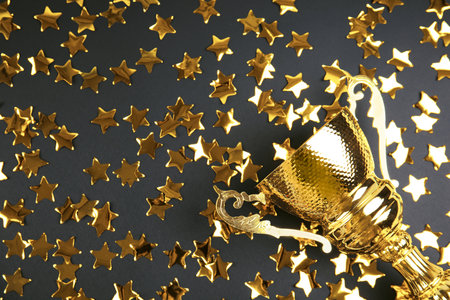Gold trophy cup and confetti on black background, flat lay. Space for textの写真素材