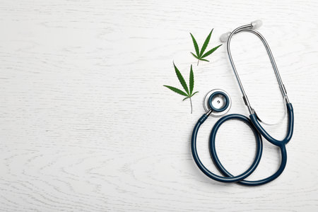 Hemp leaves and stethoscope on white wooden background, flat lay. Space for textの写真素材