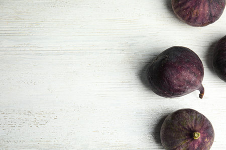 Tasty ripe figs on white wooden table, flat lay. Space for text