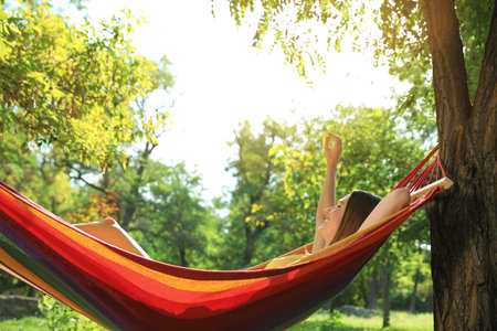 Young woman resting in comfortable hammock at green gardenの写真素材