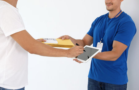Young courier with envelopes and client signing on tablet against white background, closeupの写真素材