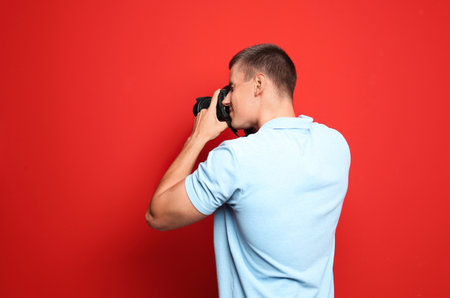 Young professional photographer taking picture on red background. Space for textの写真素材