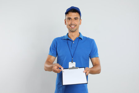 Happy young courier with clipboard on white backgroundの写真素材