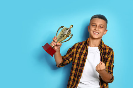 Happy boy with golden winning cup on blue backgroundの写真素材