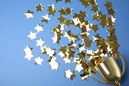 Gold trophy cup and confetti on blue background, flat lay. Space for text