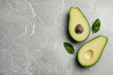 Halves of delicious ripe avocado on gray marble table, flat lay. Space for textの写真素材