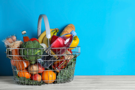 Shopping basket with grocery products on white wooden table against light blue background. Space for textの写真素材
