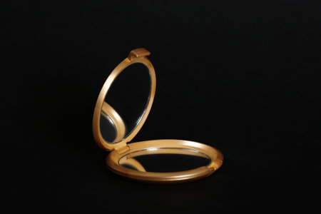 Round gold pocket mirror on black backgroundの写真素材