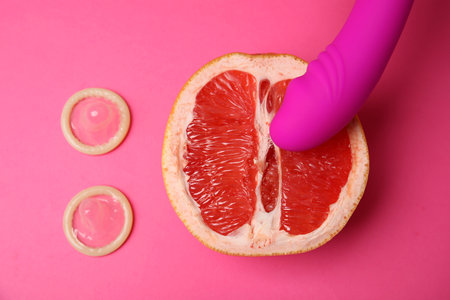 Half of grapefruit, purple vibrator and condoms on pink background, flat lay. sex conceptの写真素材