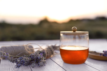 Jar with fresh honey and lavender flowers on white wooden table outdoors. Space for textの写真素材