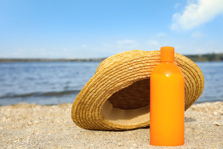Bottle of sun protection body cream and hat on beach, space for designの写真素材