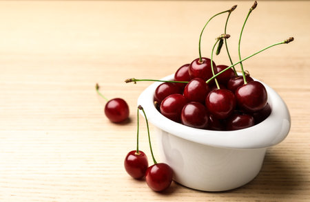 White bowl of delicious cherries on wooden table, space for textの写真素材
