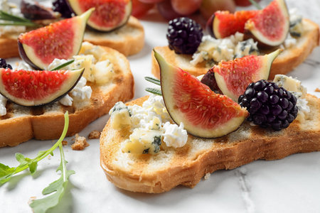 Bruschettas with cheese, figs and blackberries served on white table, closeup