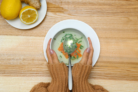 Woman with bowl of soup on wooden table, top view. Flu treatment