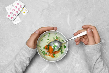 Man with bowl of soup at gray marble table, top view. Flu treatment