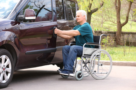 Mature man in wheelchair opening door of his van outdoorsの写真素材