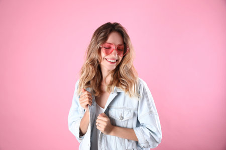 Young beautiful woman wearing heart shaped glasses on pink backgroundの写真素材