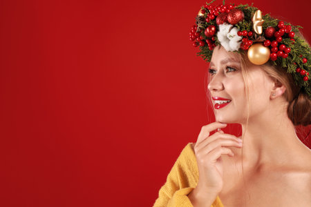 Beautiful young woman wearing Christmas wreath on red background. Space for textの写真素材