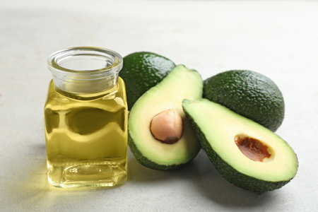 Jar of natural oil and avocados on gray stone background