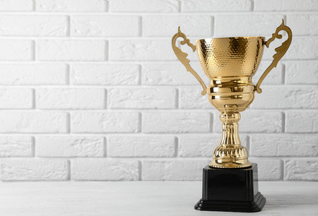 Golden trophy cup on table near white brick wall. Space for textの写真素材