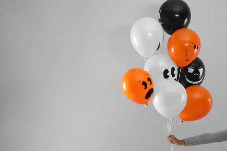 Woman holding color balloons for Halloween party on light gray background, closeup. Space for textの写真素材