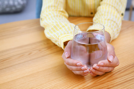 Woman holding glass of water at wooden table, closeup with space for text. Refreshing drinks