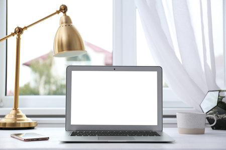 Modern laptop on desk near window at homeの写真素材