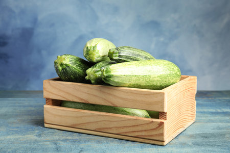 Wooden crate with fresh ripe green zucchinis on table against blue backgroundの写真素材