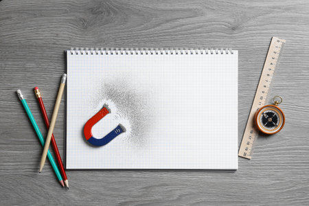 Notebook, stationery, compass and magnet with iron powder on wooden table, flat lay. Space for textの写真素材