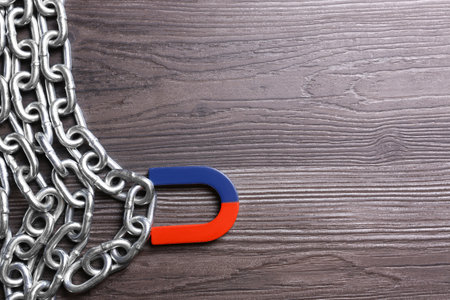 Magnet attracting chain on dark gray wooden background, flat lay. Space for text