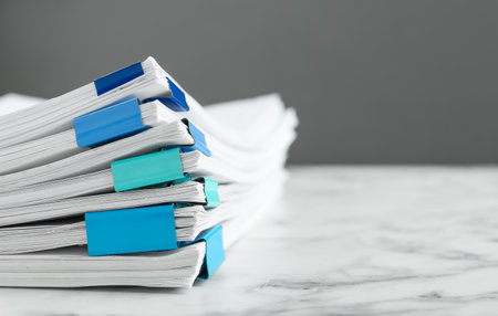 Stack of documents with binder clips on marble table against gray background, closeup. Space for...