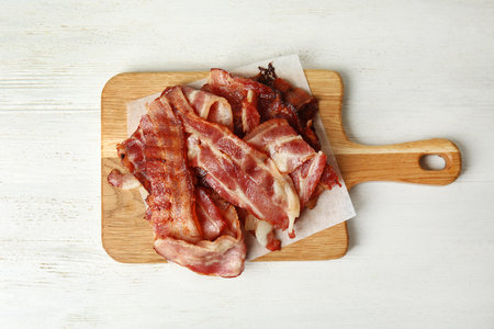 Slices of tasty fried bacon on white wooden table, top view