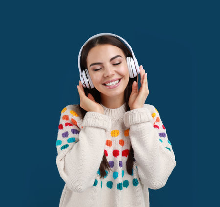 Young woman listening to music with headphones on dark blue background, space for textの写真素材