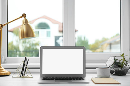 Modern laptop on desk near window at homeの写真素材