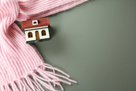 Wooden house model and pink scarf on gray background, top view with space for text. heating efficiencyの写真素材